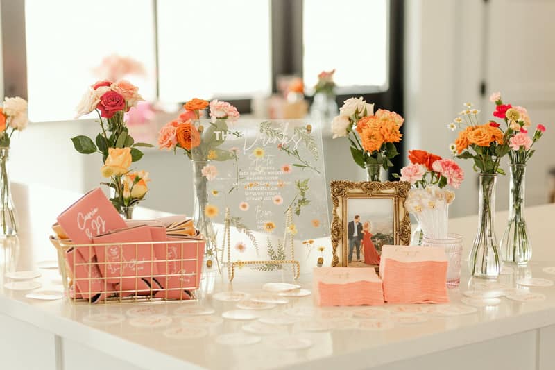 Bar welcome table dressed with bright florals and personalized koozies