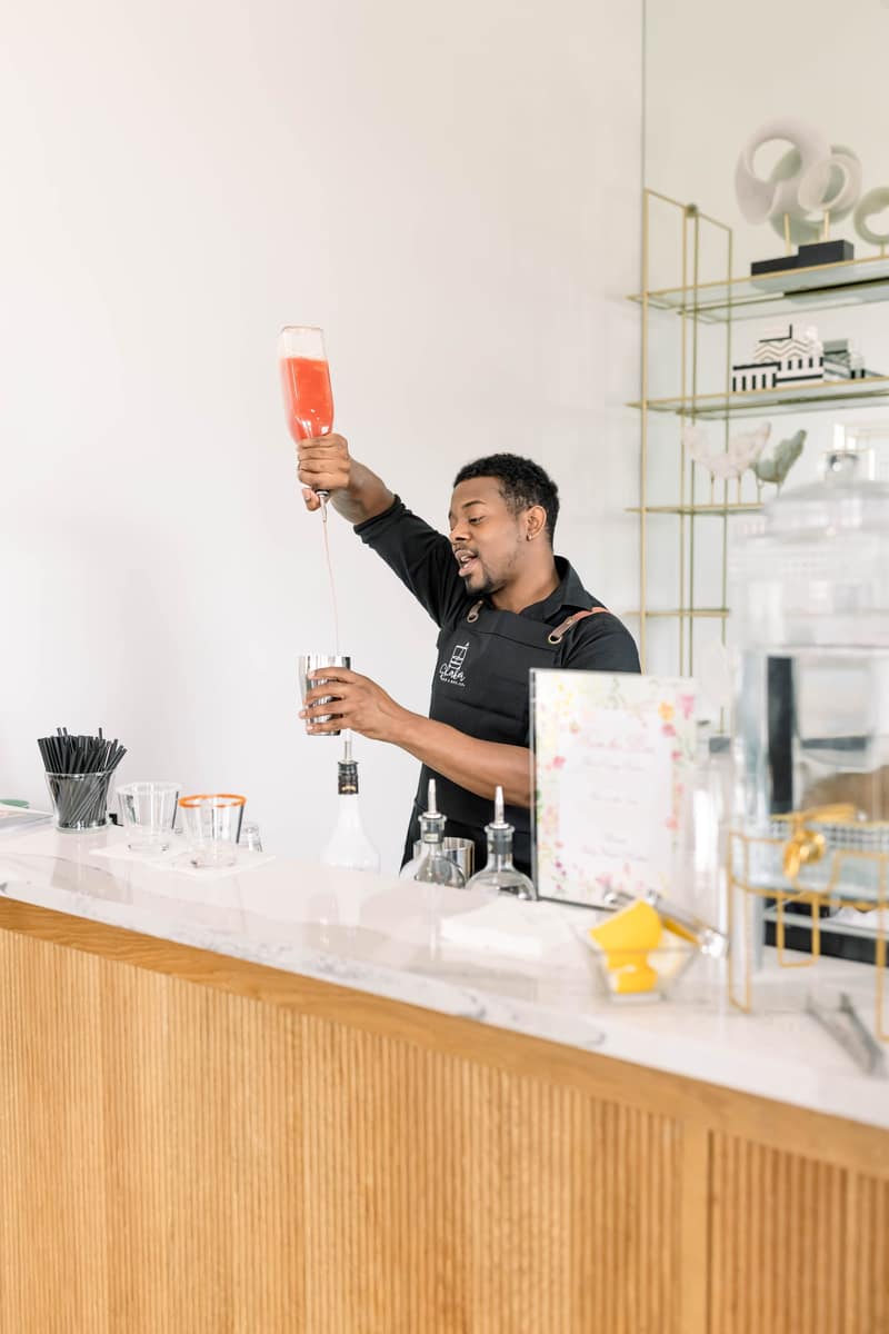 Shaker bartender pouring a cocktail from height into a metal shaker tin at a marble bar