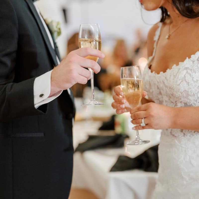 Close-up of a bride and groom's hands touching champagne flutes together