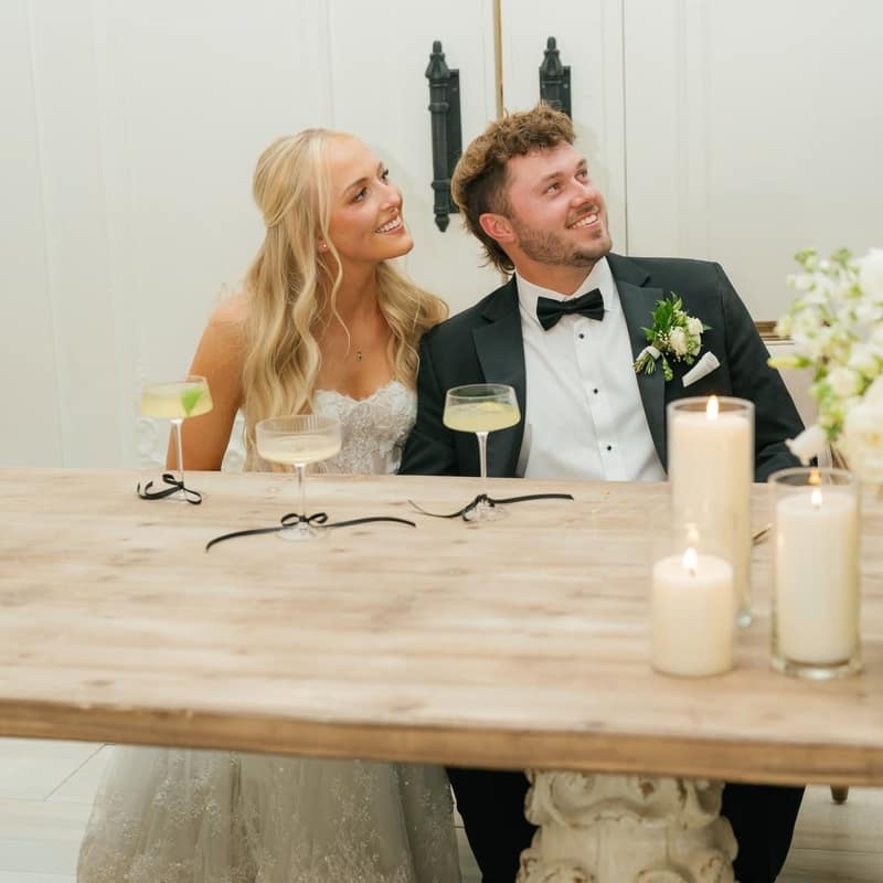Bride and groom at their sweetheart table with a pair of coupe cocktails and lit candles