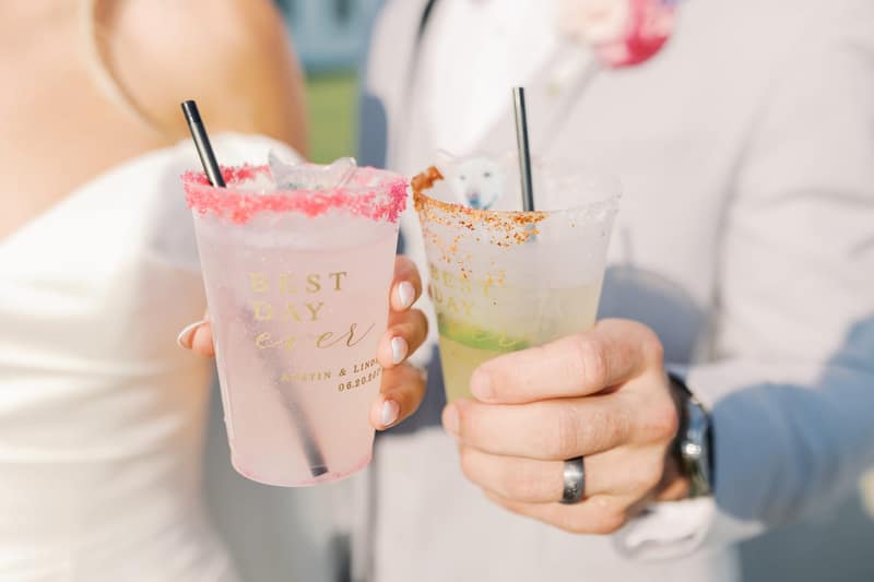 Two personalized 'Best Day Ever' wedding cups, one with a pink glitter rim and one with a chili-salt rim, each garnished with a cat- or dog-shaped ice cube