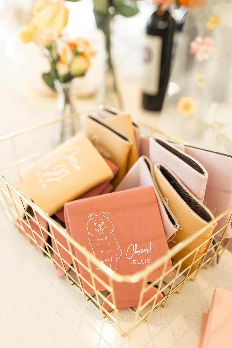 Personalized wedding koozies in a gold basket on a bar detail table