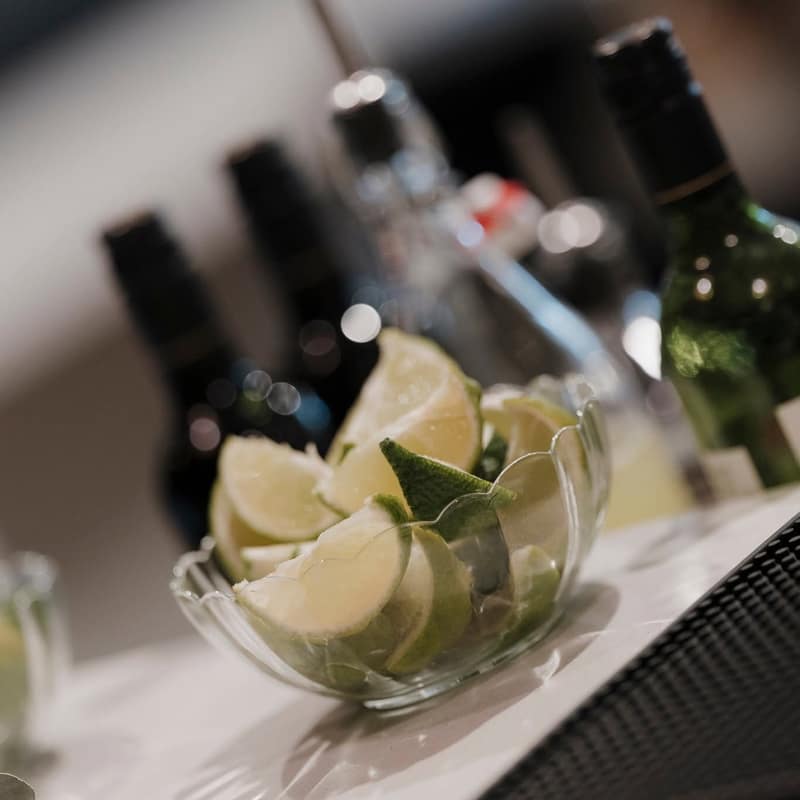 Bowl of cut limes on the bar with spirit bottles and pour spouts lined up behind